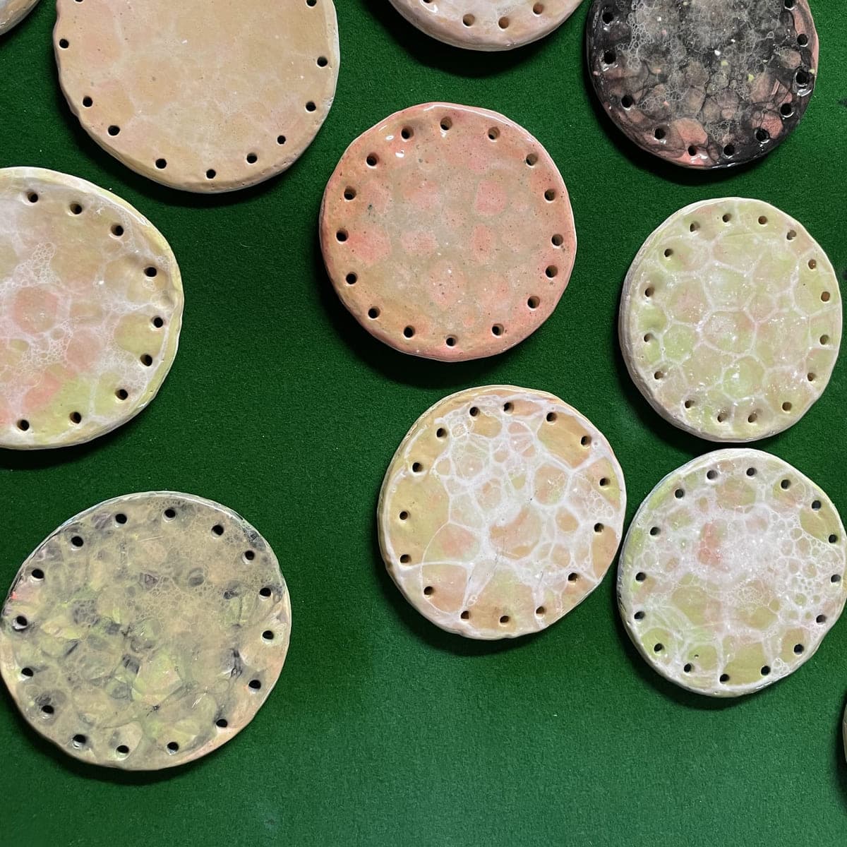Small round clay discs with pierced edges, laid out on green baize
