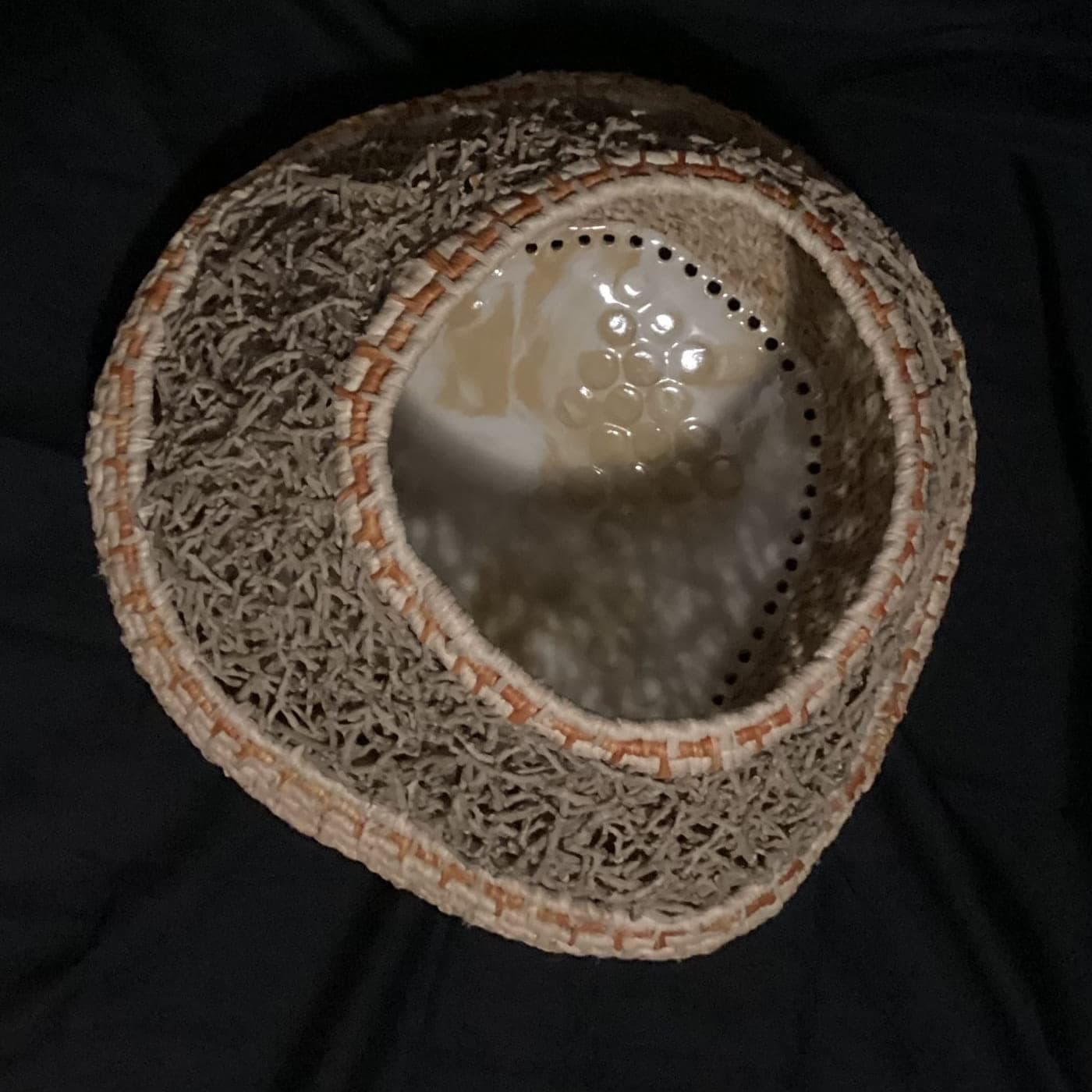 Coiled fibre vessel with a glazed centre, photographed against black