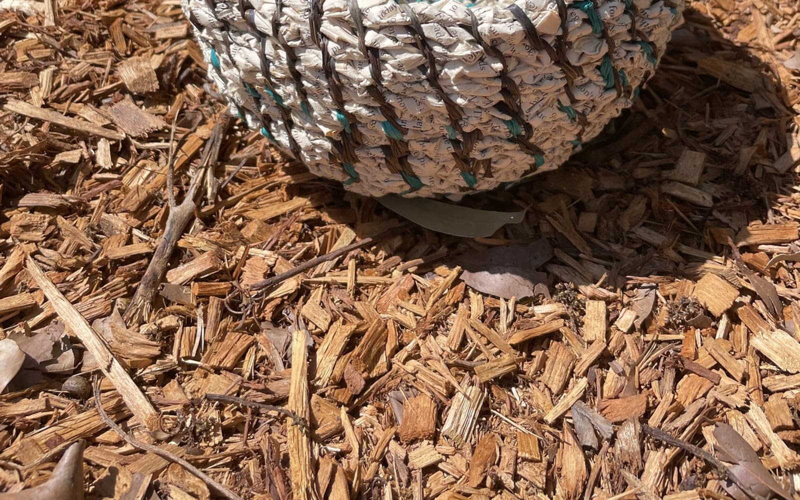 A coiled bowl in grey and cream resting on garden mulch