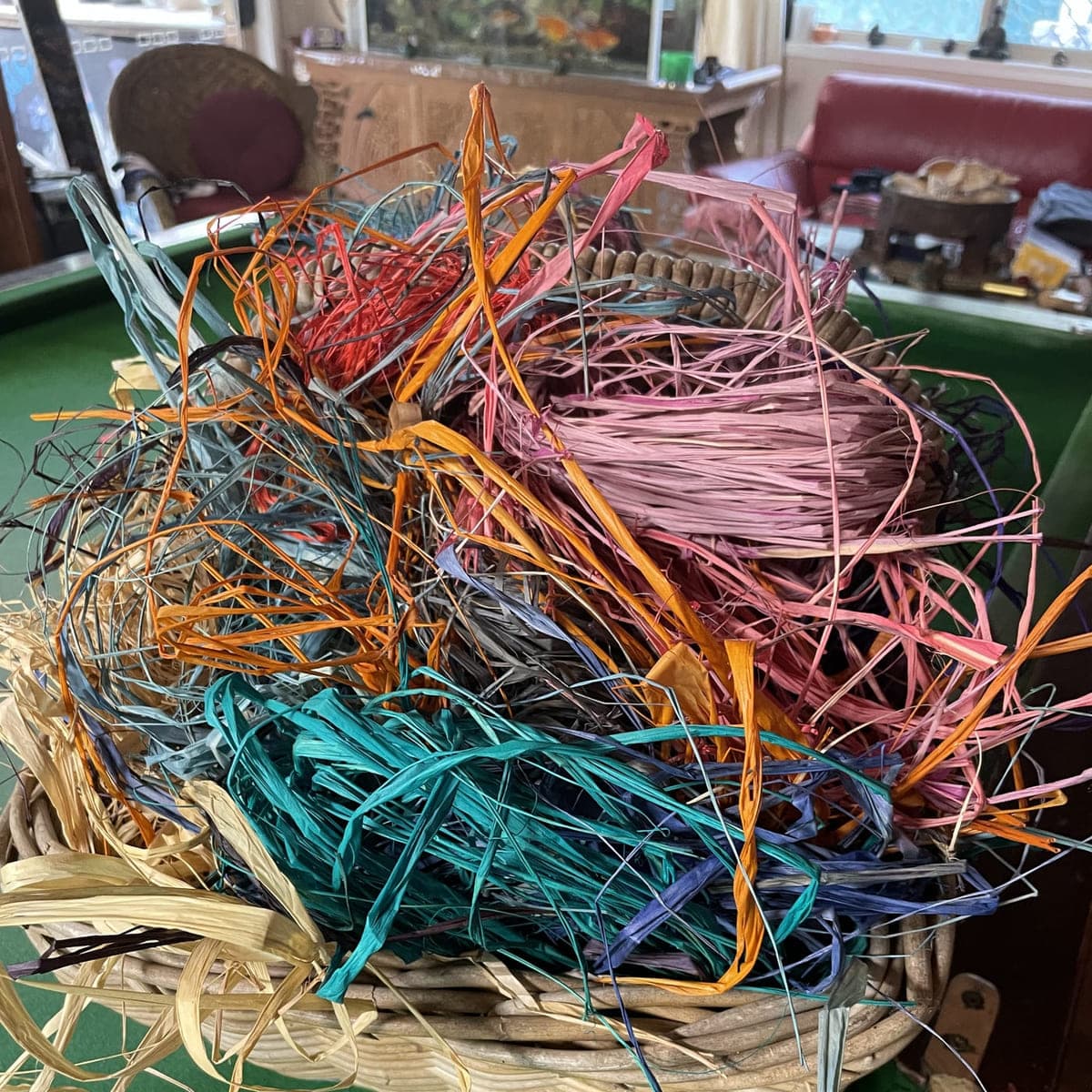 A basket heaped with dyed raffia offcuts in many colours